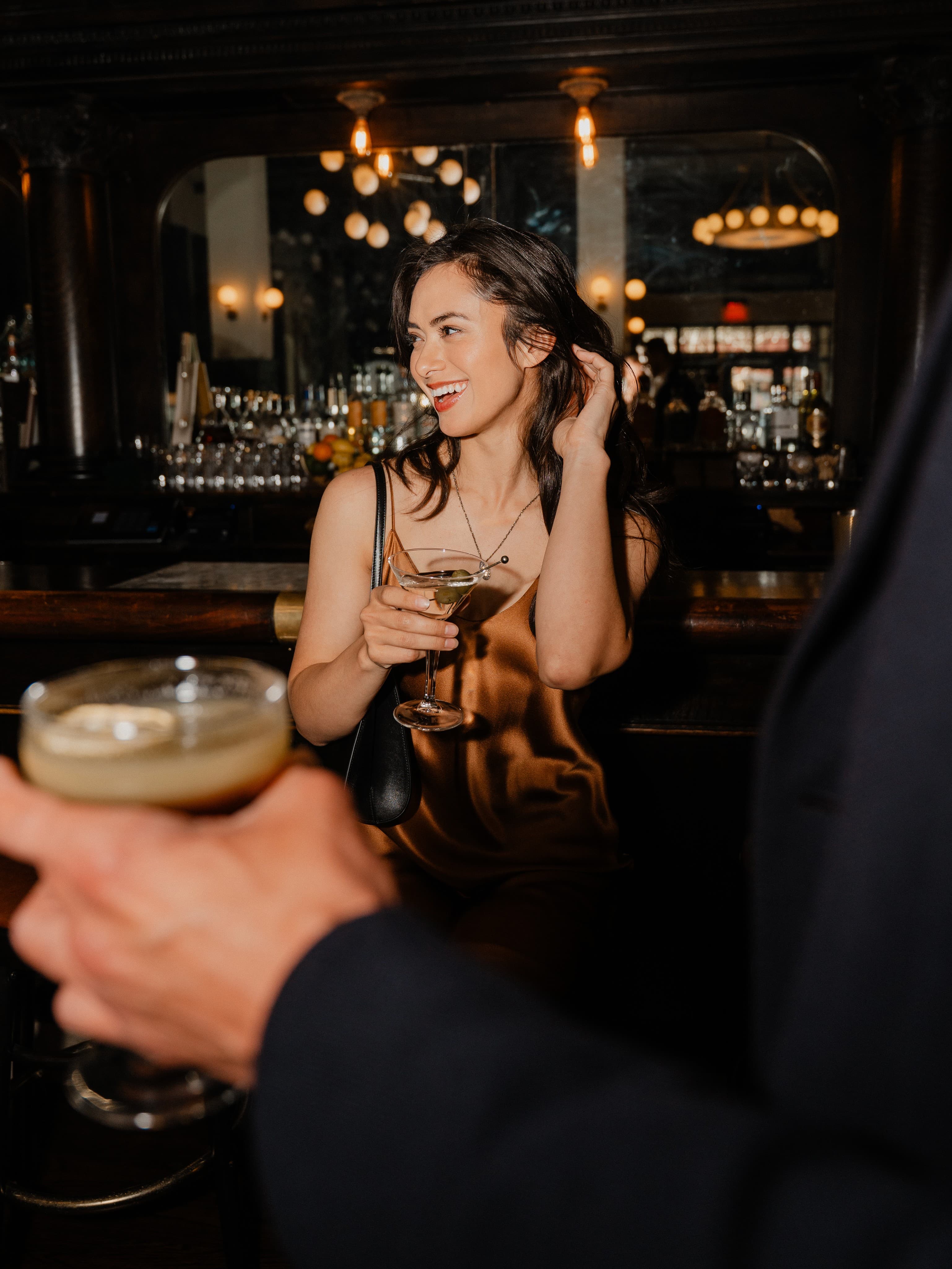 Woman laughing at a bar holding a cocktail